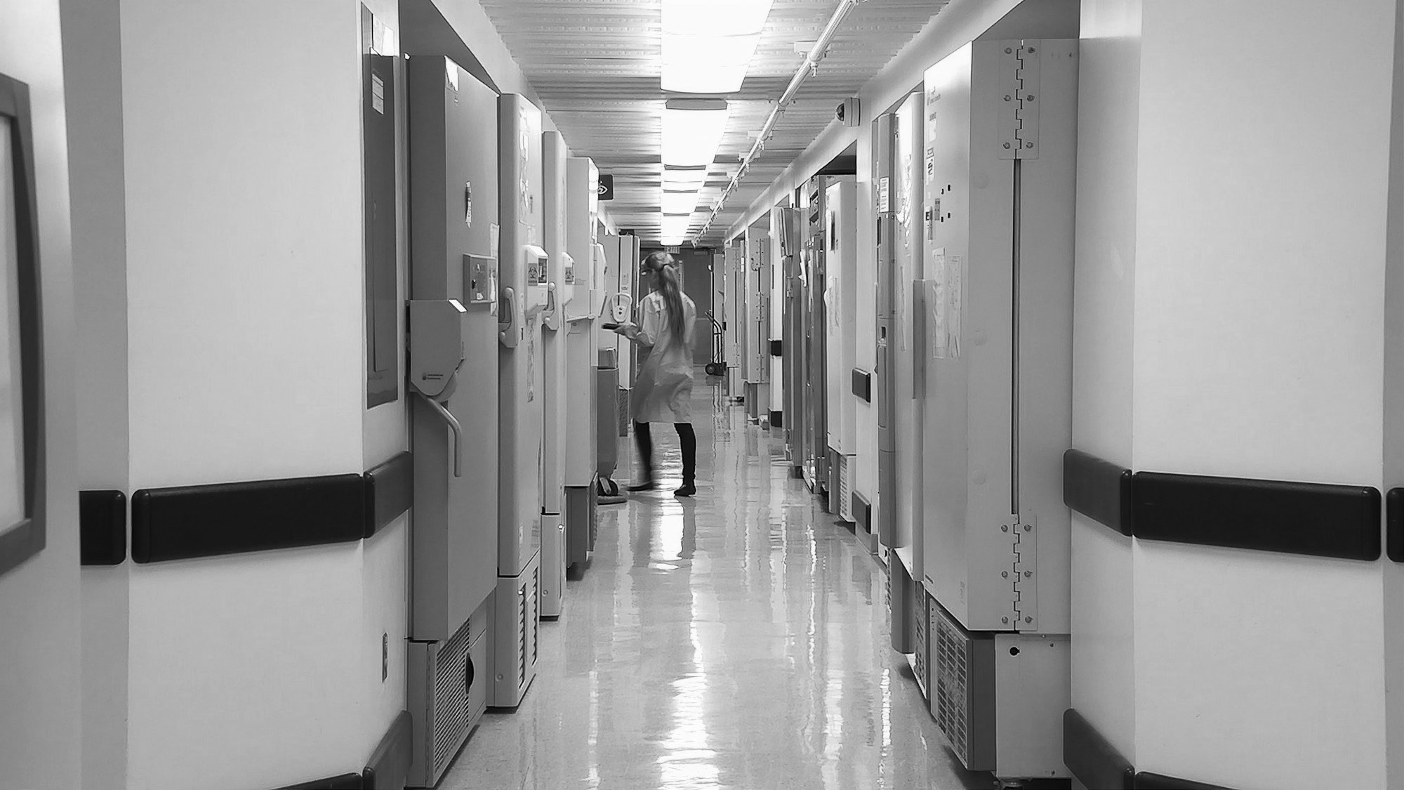A long clinical corridor lined with equipment, with a person in a lab coat at the far end